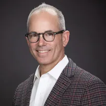 Professional headshot of man with glasses in plaid jacket