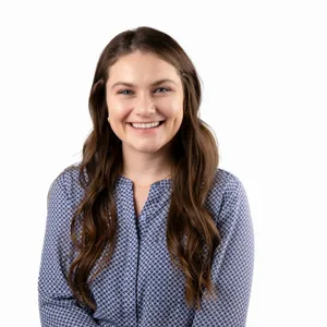 Professional headshot of a young woman with long brown hair wearing a blue patterned blouse
