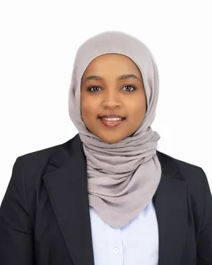 Professional headshot of a young woman wearing a light gray hijab and black blazer over a white shirt
